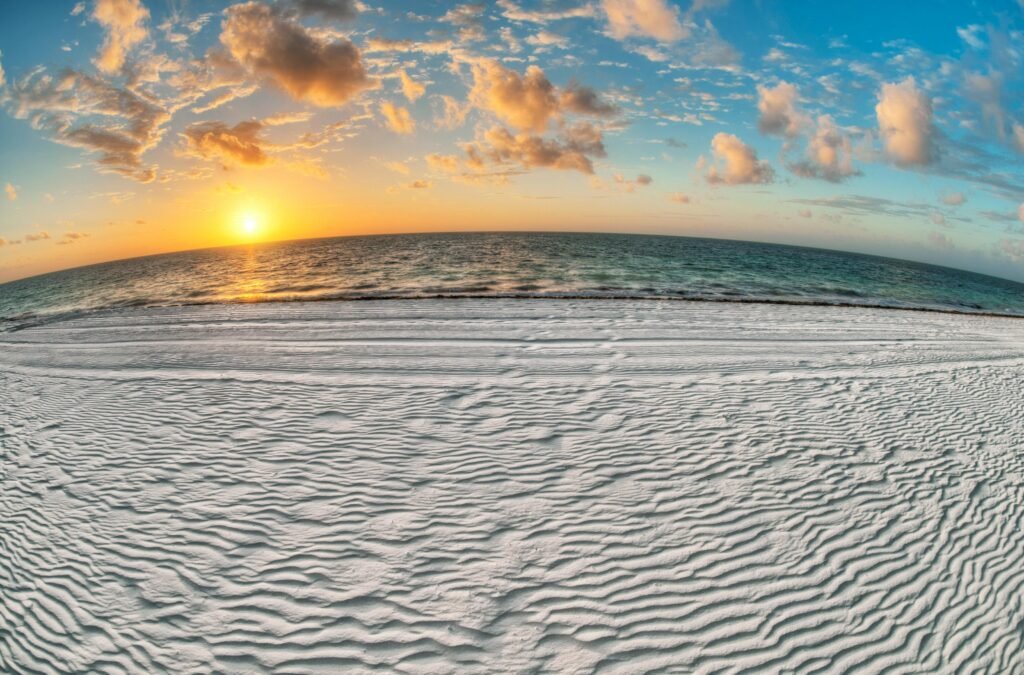Experience the tranquil beauty of a beach sunrise with golden sun, soft sand, and scattered clouds over the ocean.